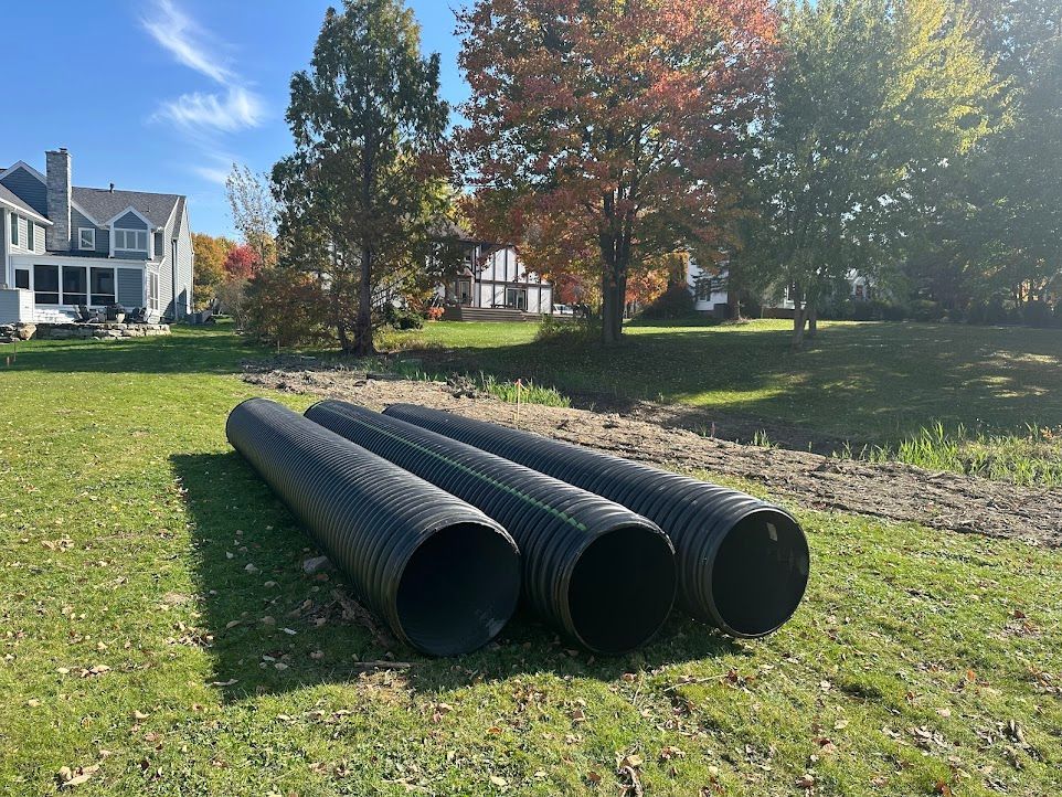 Three black pipes are stacked on top of each other in a grassy field.