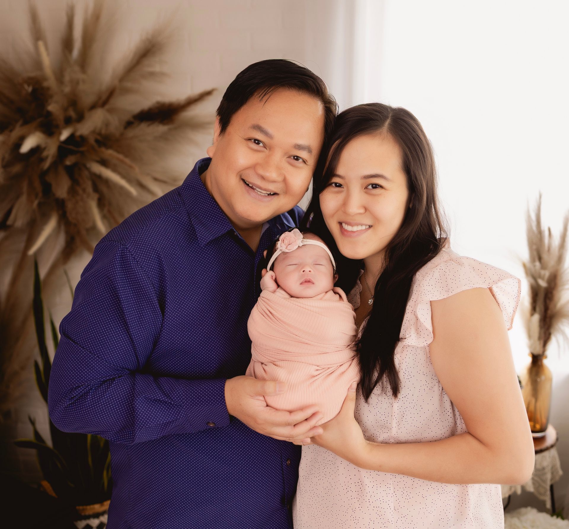 Dr. John Vu Ho smiling with Thea and Anna. Parents holding newborn baby wrapped in pink blanket.