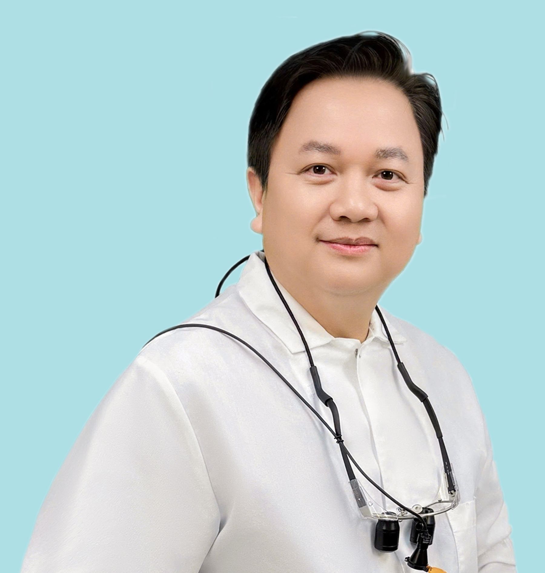 Smiling Dr. John Vu Ho man in white coat, wearing dental loupes, against a light blue background.