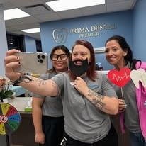 Three people posing for a photo in a dental office. One holds a fake mustache, the others hold props.