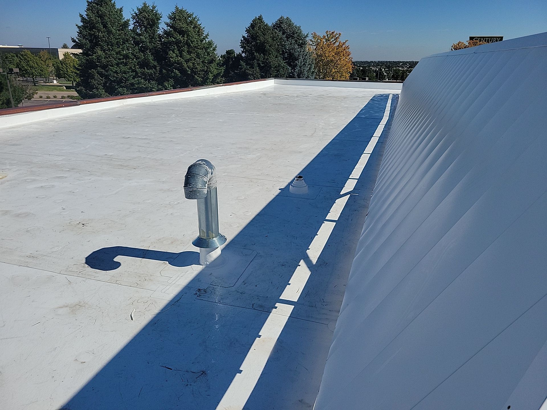 A white roof with a pipe on it and trees in the background.
