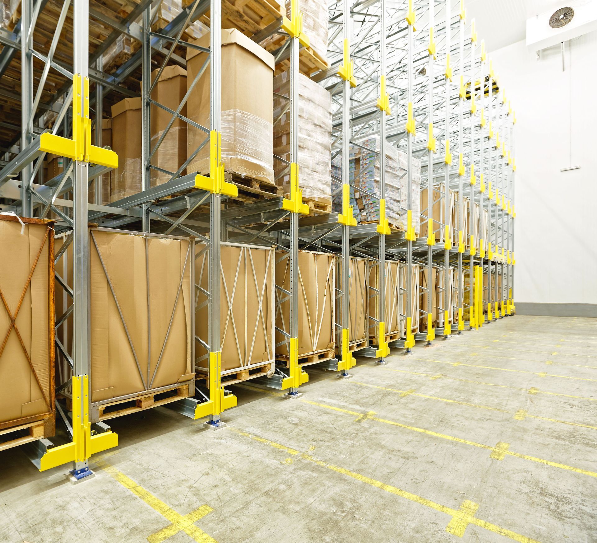 Warehouse racks stacked with large cardboard boxes and yellow safety supports in a bright storage aisle
