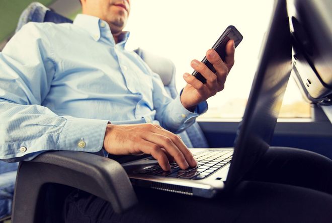 Person in a blue shirt using a laptop and checking a smartphone in an office chair