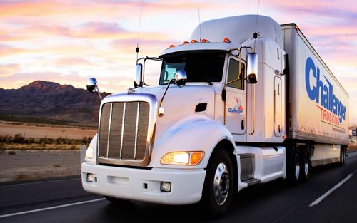 White Challenger Trucking delivery truck driving on a desert road at sunset