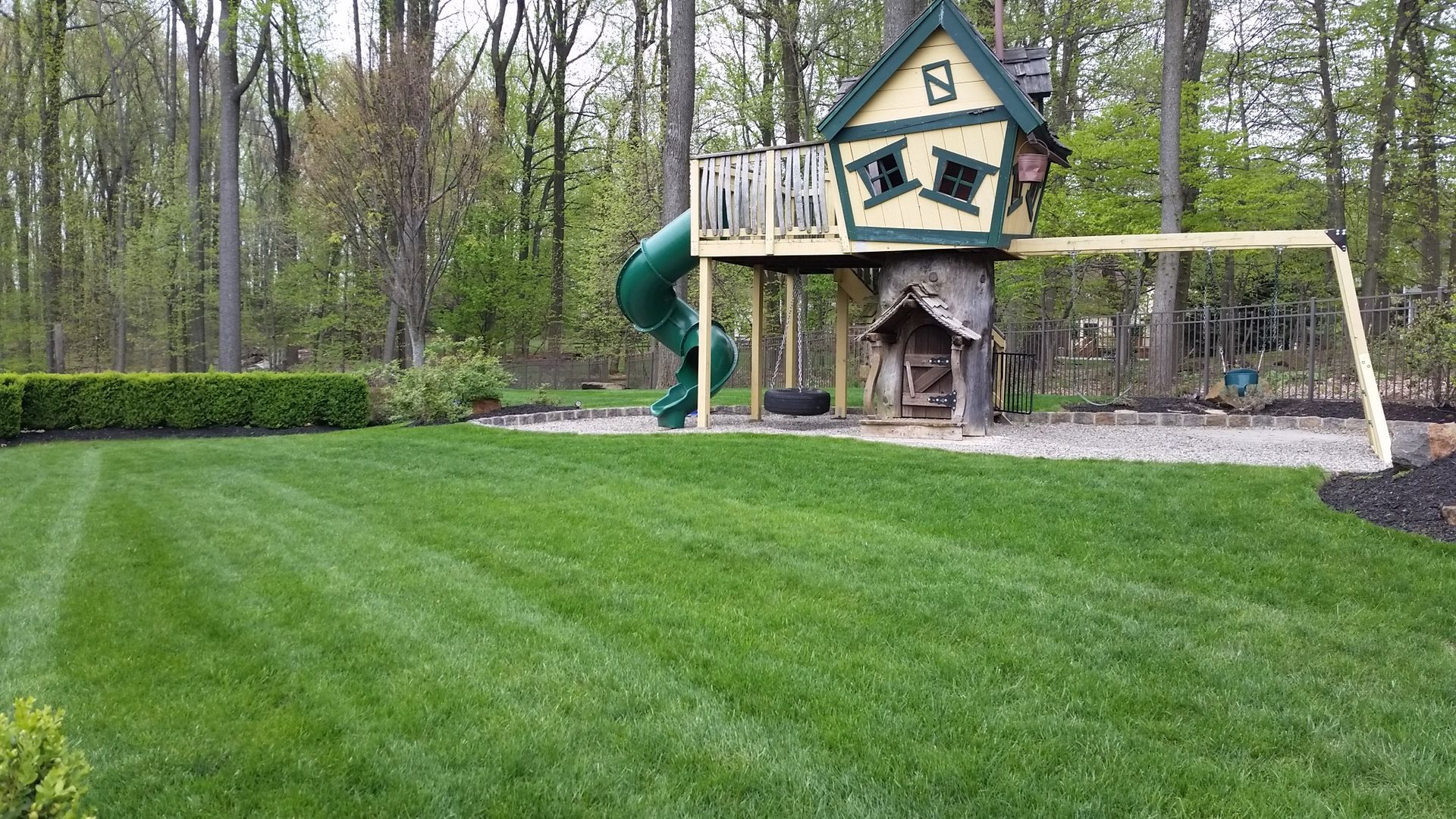 A tree house with a slide and swings in a backyard.