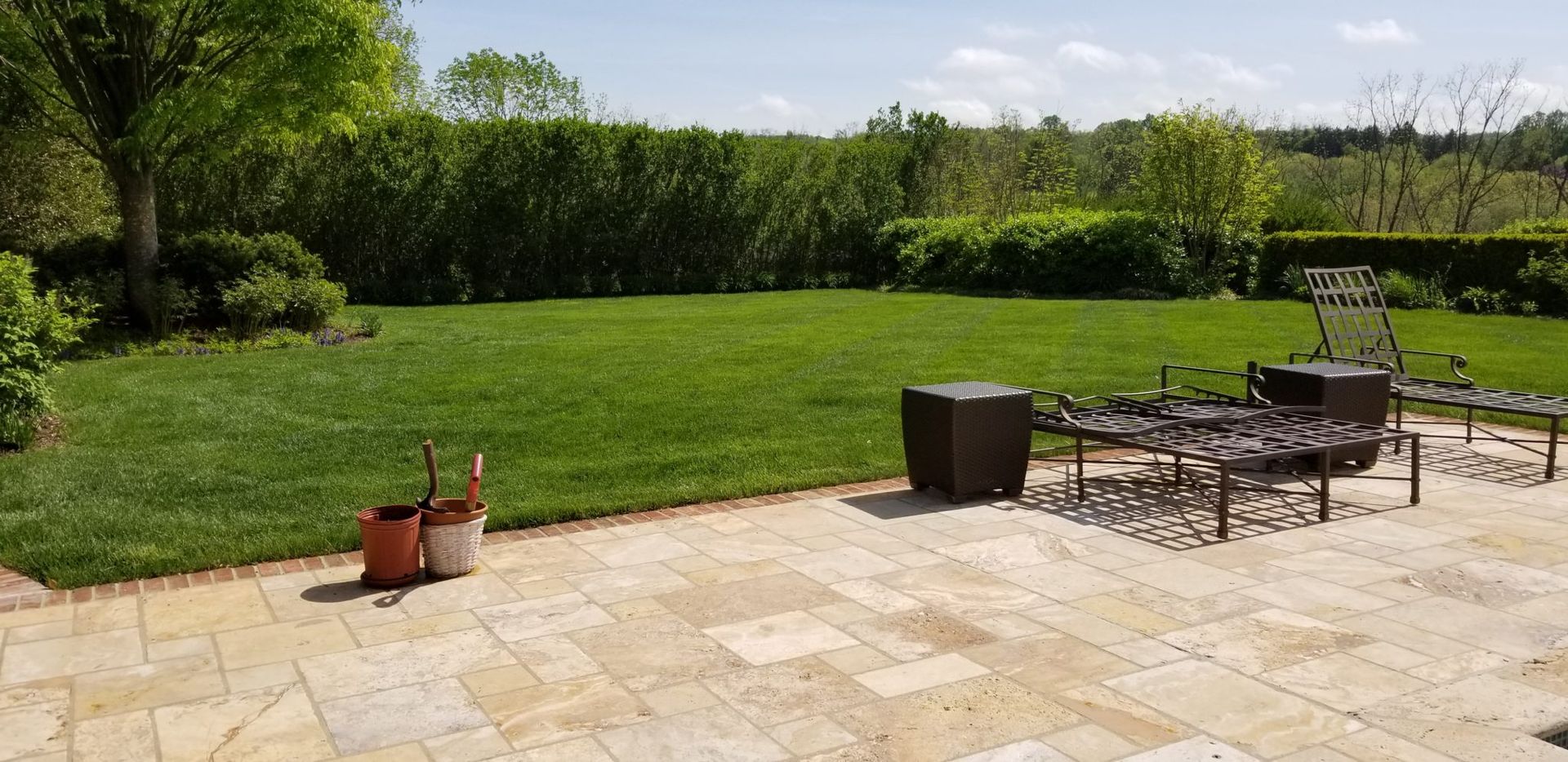 A patio with chairs and potted plants in front of a large lush green lawn.