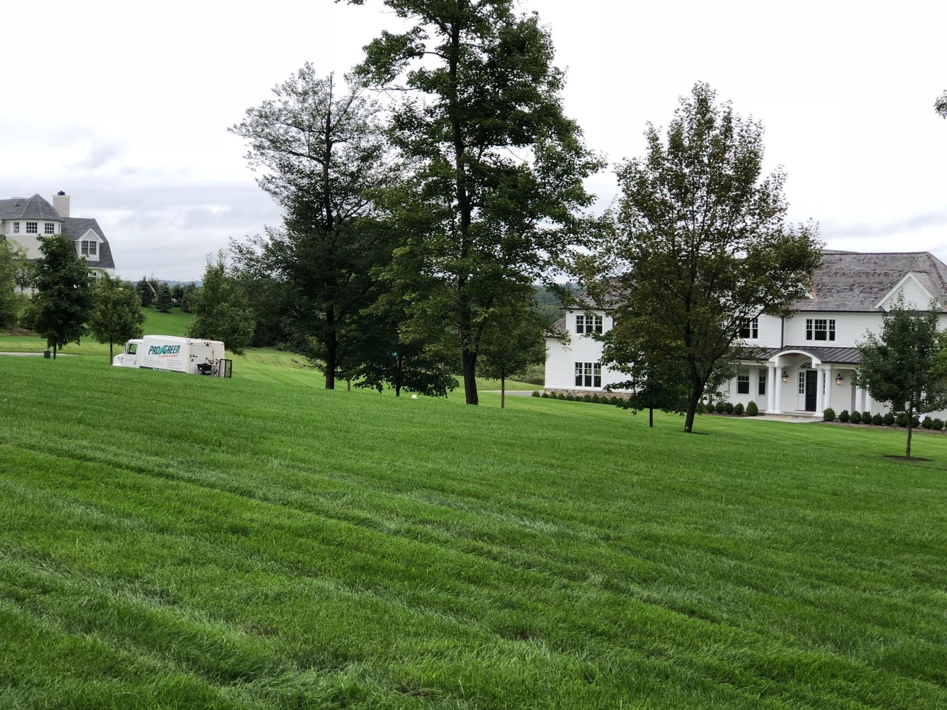 A large white house is sitting in the middle of a lush green field.