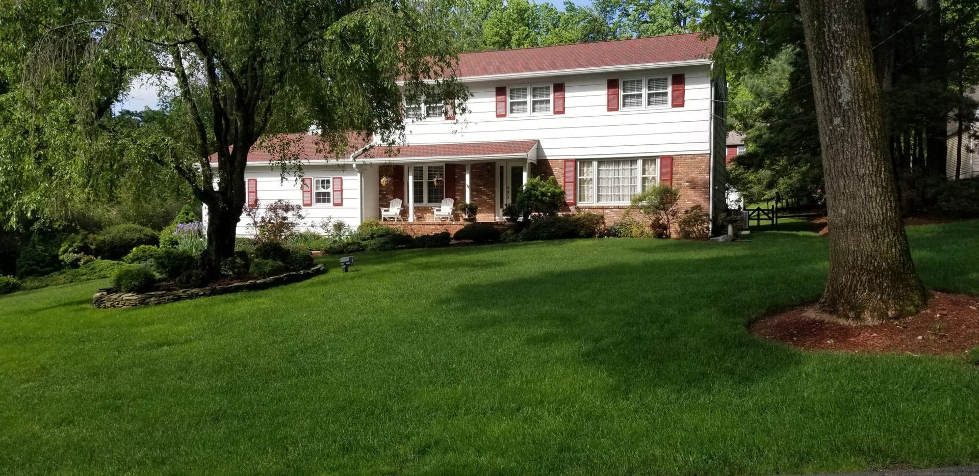 A white house with red shutters and a large lawn in front of it.