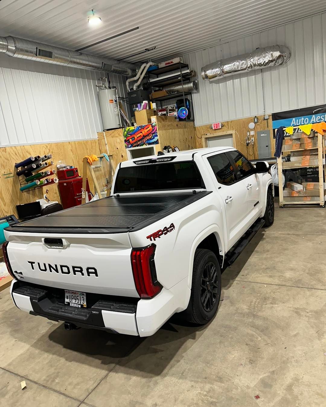 A white truck with a black bed cover is parked in a garage.