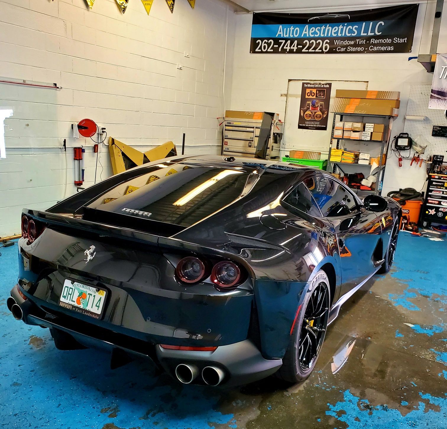 A black sports car is parked in a garage with a sign above it that says auto aesthetics llc