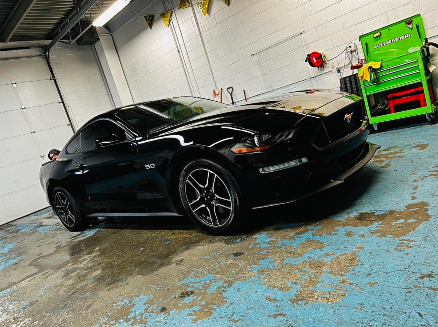 A black mustang is parked in a garage next to a green tool cart.