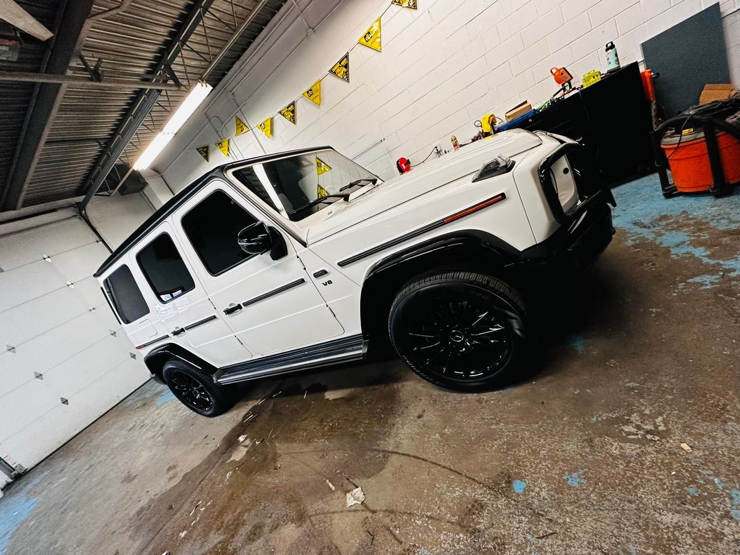 A white mercedes benz g63 is parked in a garage.