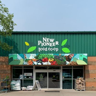 New Pioneer Food Co-op storefront with produce mural and green awning, under a blue sky.