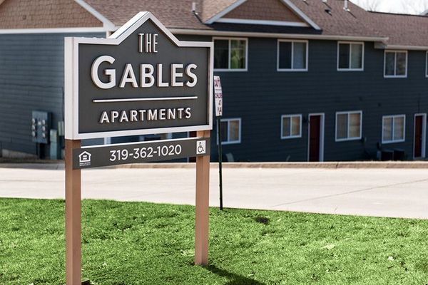 Sign for The Gables Apartments, dark blue building in the background. Phone number is 319-362-1020.