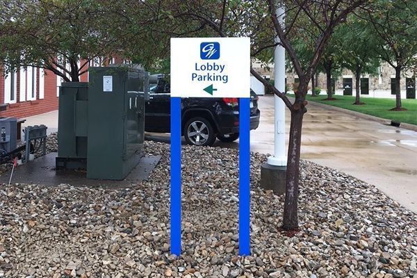 Sign for Lobby Parking, white and blue, with a green arrow, on a gravel bed.