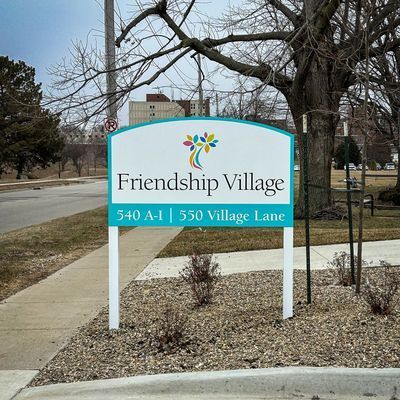 Sign for Friendship Village, a retirement community. Blue, white sign with logo, text, addresses.