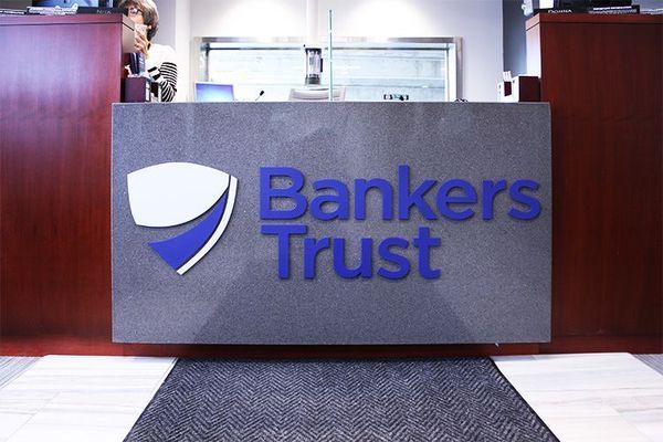 Bankers Trust bank counter with logo, dark wood, blue lettering, and a person partially visible behind the counter.