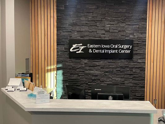 Reception area: desk with sign for Eastern Iowa Oral Surgery & Dental Implant Center, black stone wall, wooden paneling.