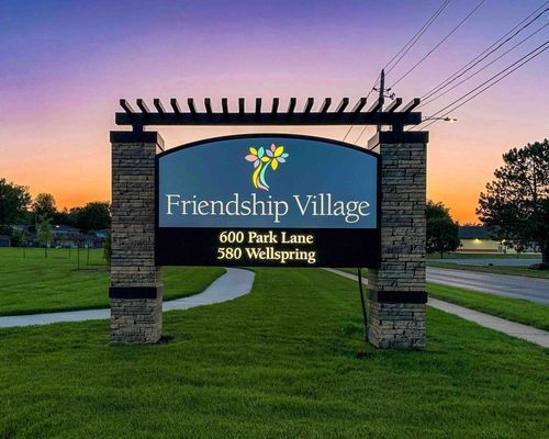 Sign for Friendship Village, with logo, address, and dusk sky backdrop.