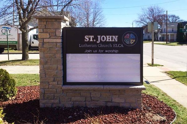 Sign for St. John Lutheran Church, BLCA with a changeable message board, surrounded by brick and stone.