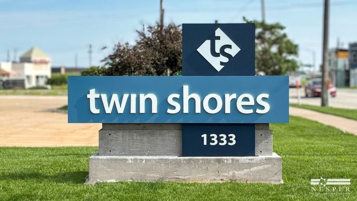 Twin Shores sign with logo, address 1333, in front of grass and road.