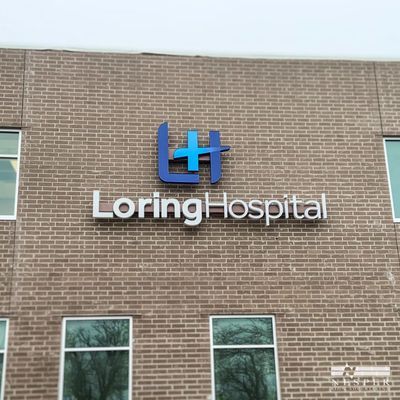 Loring Hospital sign on a brick building with windows; a blue and cyan logo above the name.