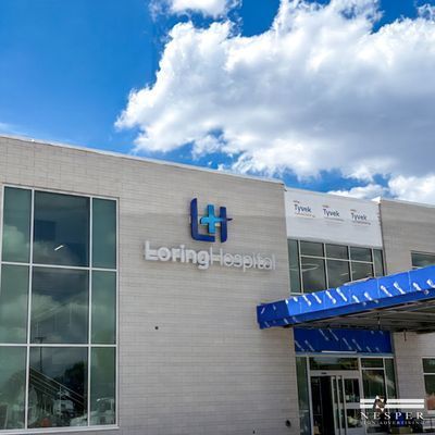 Loring Hospital exterior with blue logo, modern building, bright sky.