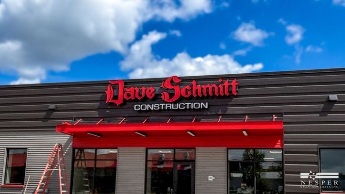 Sign for Dave Schmitt Construction in red lettering; a building with a red awning.