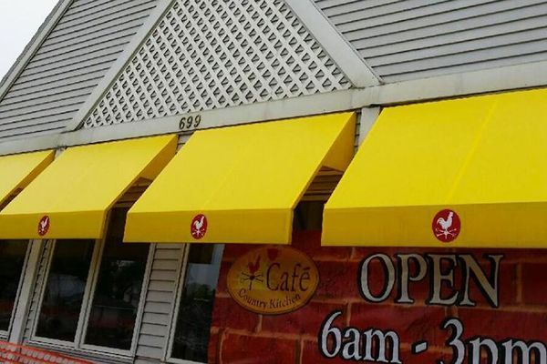 Yellow awnings over a cafe, with red logo, OPEN sign, and brick facade.
