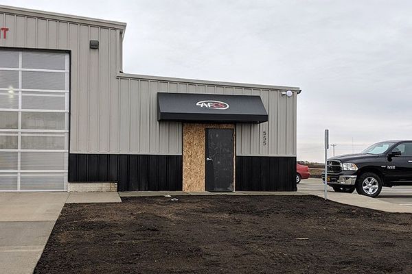 Exterior view of a commercial building with a rollup door and a black awning over a door, a black pickup truck parked nearby.