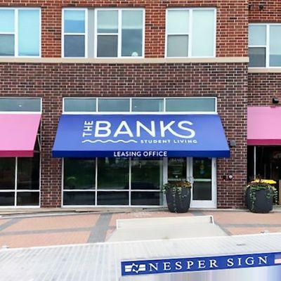 The Banks Student Living leasing office exterior with blue awning, brick building, and potted plants.