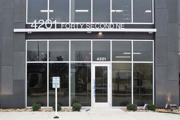 Exterior of a building with glass windows and door, address 4201 Forty Second NE. A parking sign is in front.