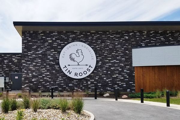 Sign for Tin Roost restaurant. White circle with rooster logo on dark brick building.