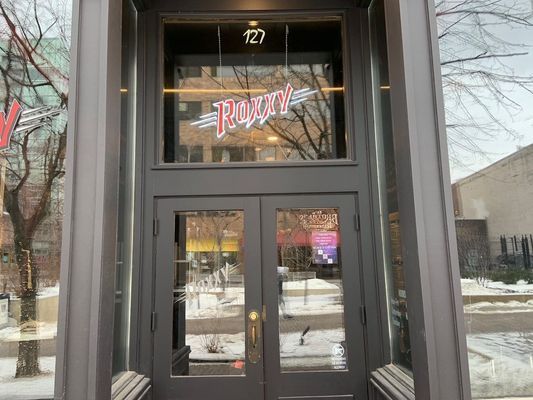 Gray doorway with glass doors and a window above. Sign reads 