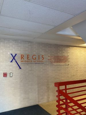 Sign for Regis Middle School on a brick wall, stairs with red railing visible.