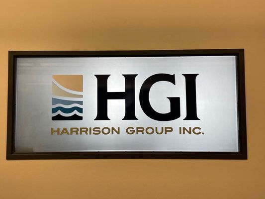 Sign for Harrison Group Inc. with logo and company name in black text on a silver background, framed.