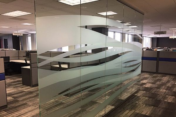 Glass office partition with frosted wave design, separating cubicles.