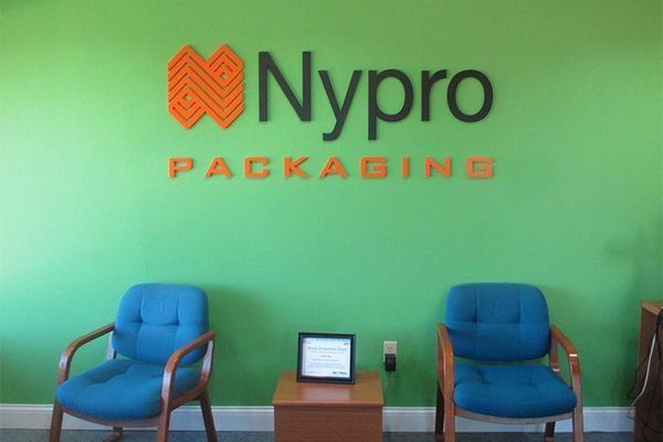 Green wall with Nypro Packaging logo above two blue chairs.
