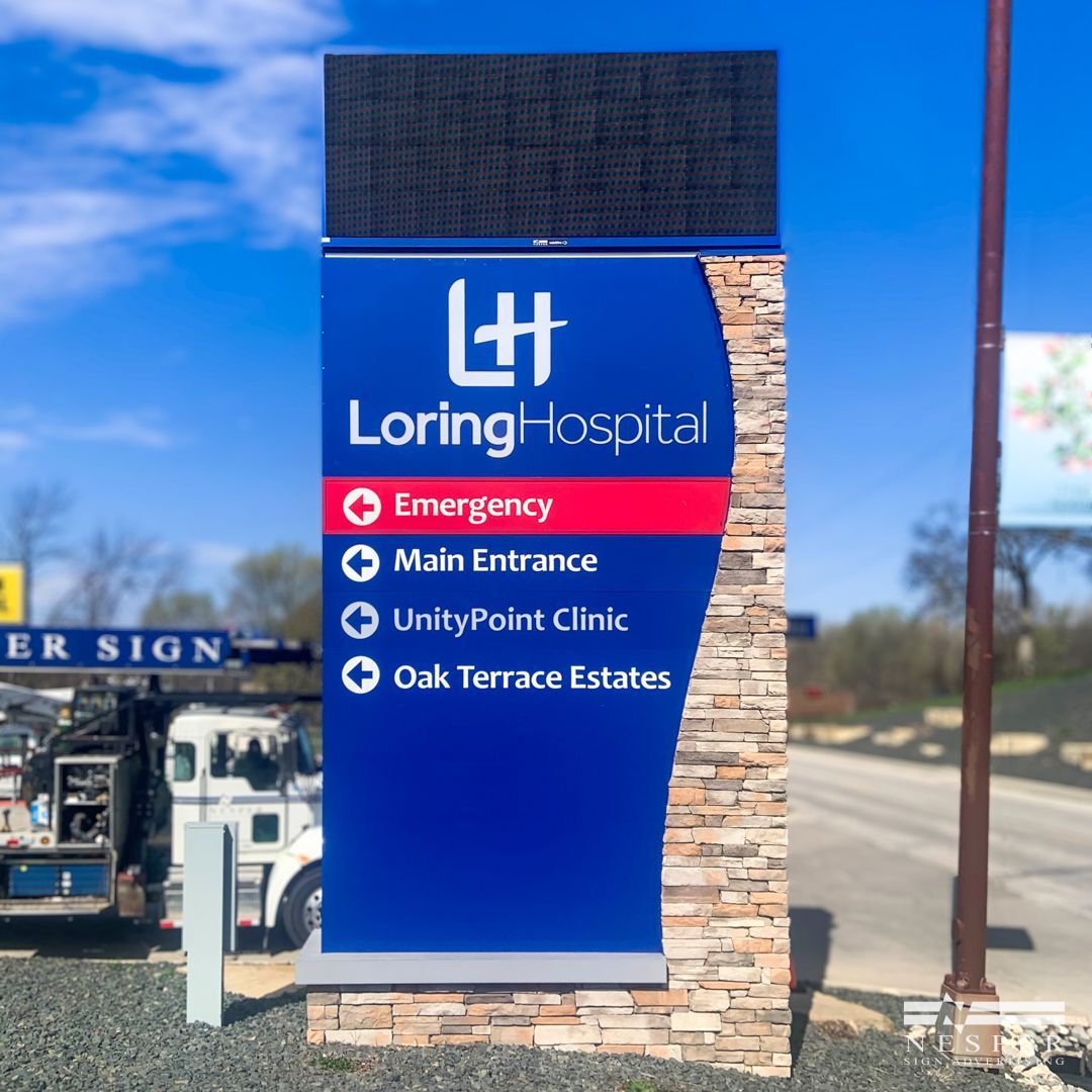 Loring Hospital sign with directions. Blue sign, red emergency section, brown stone facade, LED display at top.
