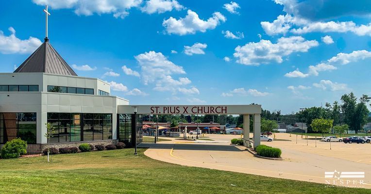 St. Pius X Church with entrance archway on a sunny day with blue sky and white clouds.