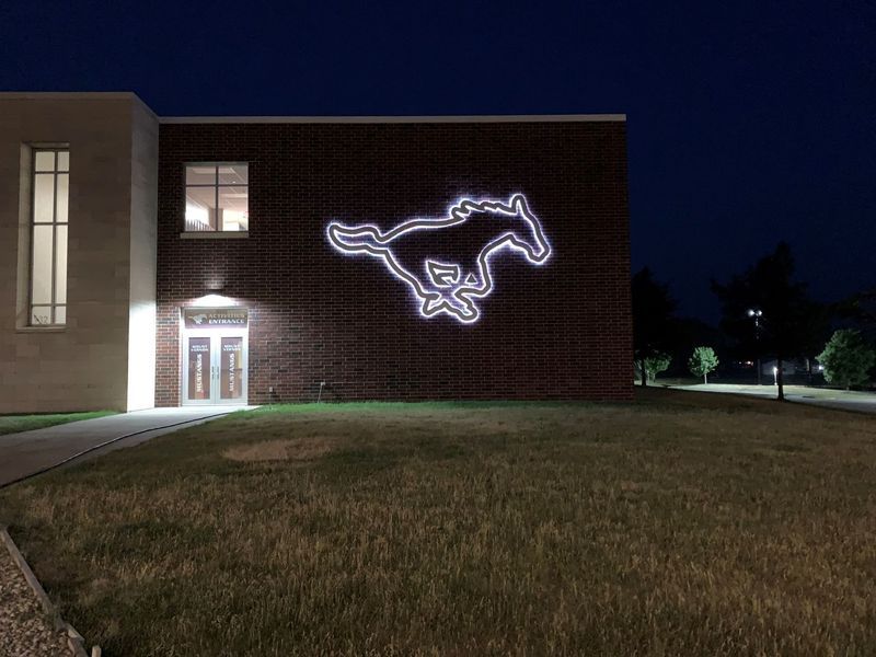 Night view of brick building with illuminated mustang logo. Grass lawn in front.