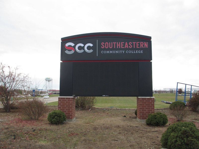 Sign for Southeastern Community College, black with red and white lettering, on brick pillars, outdoors.
