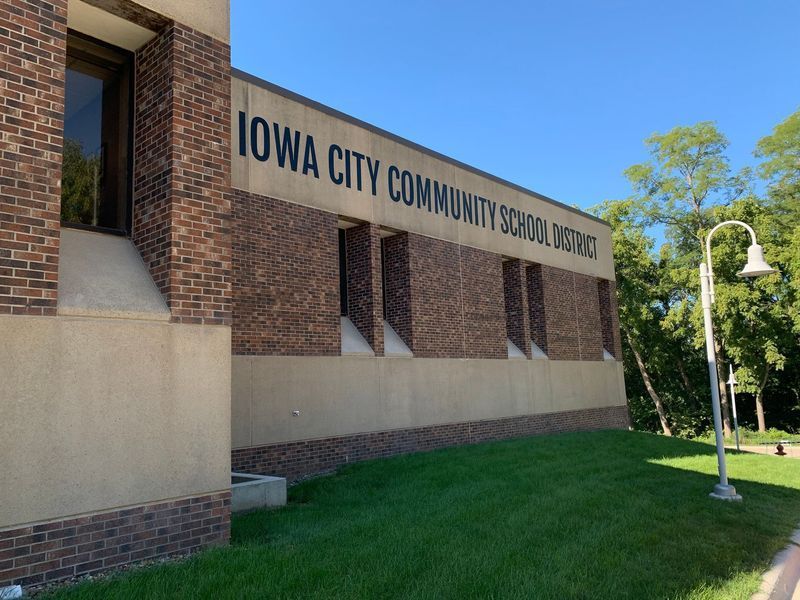 Exterior of the Iowa City Community School District building; brick and tan walls, green lawn, blue sky.