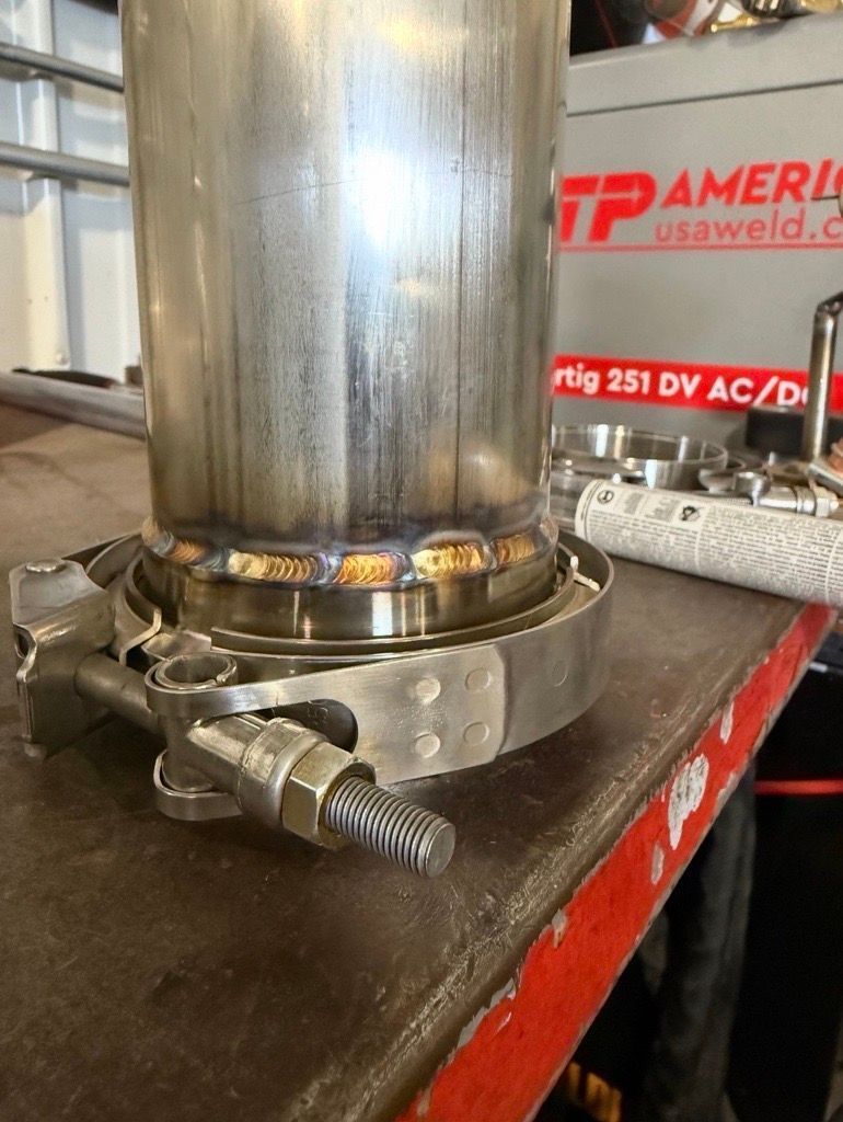 Welded stainless steel pipe on a workbench, secured with clamps in a metal shop.