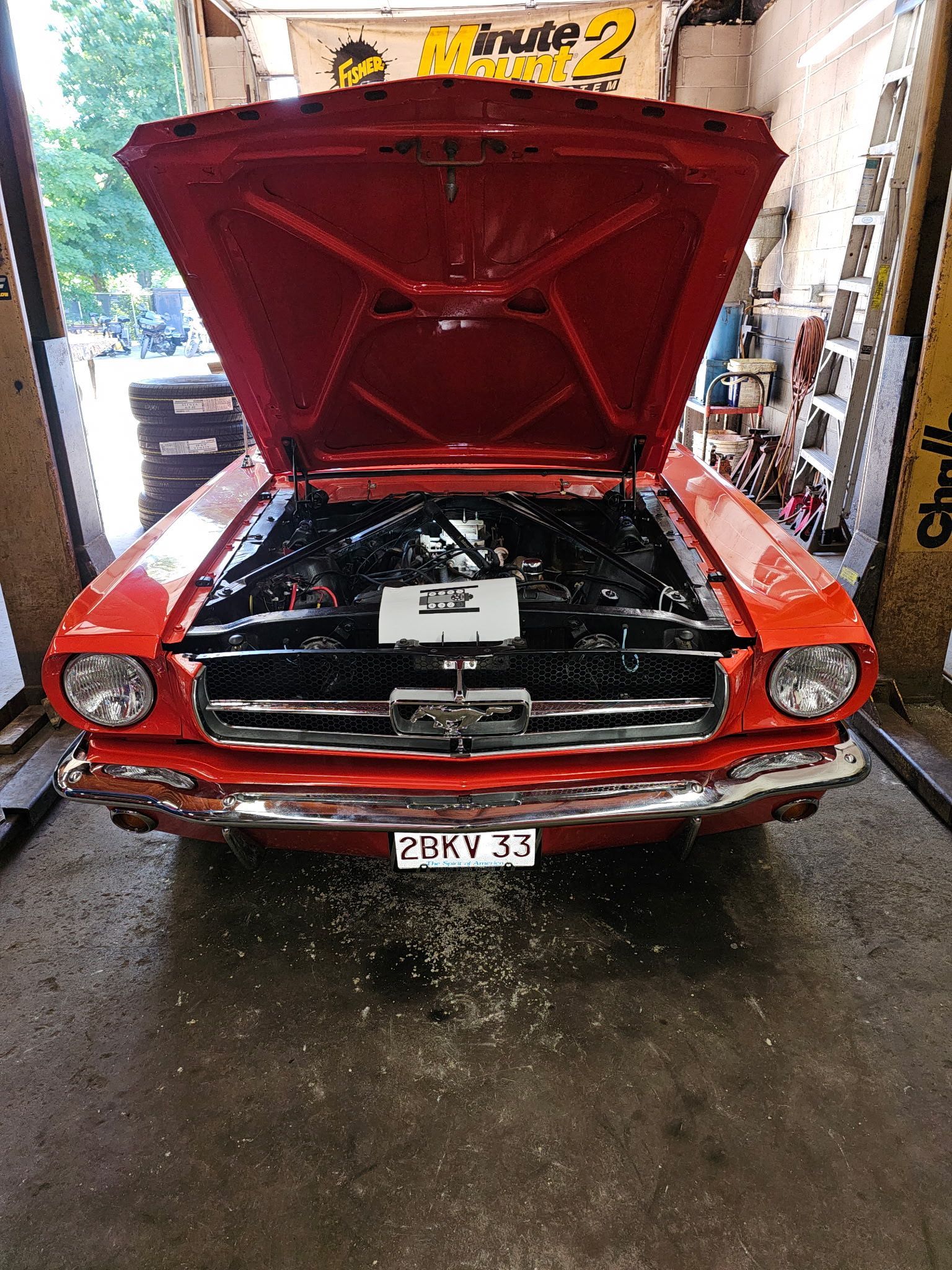 Red classic car with hood open, showing engine in a garage.