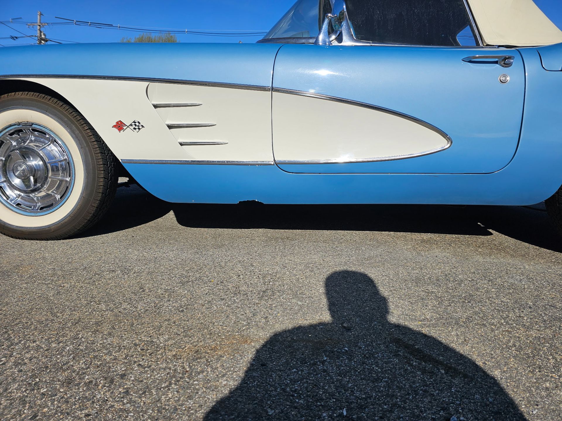 Blue classic car side view with white flame decal, parked on pavement in sunlight