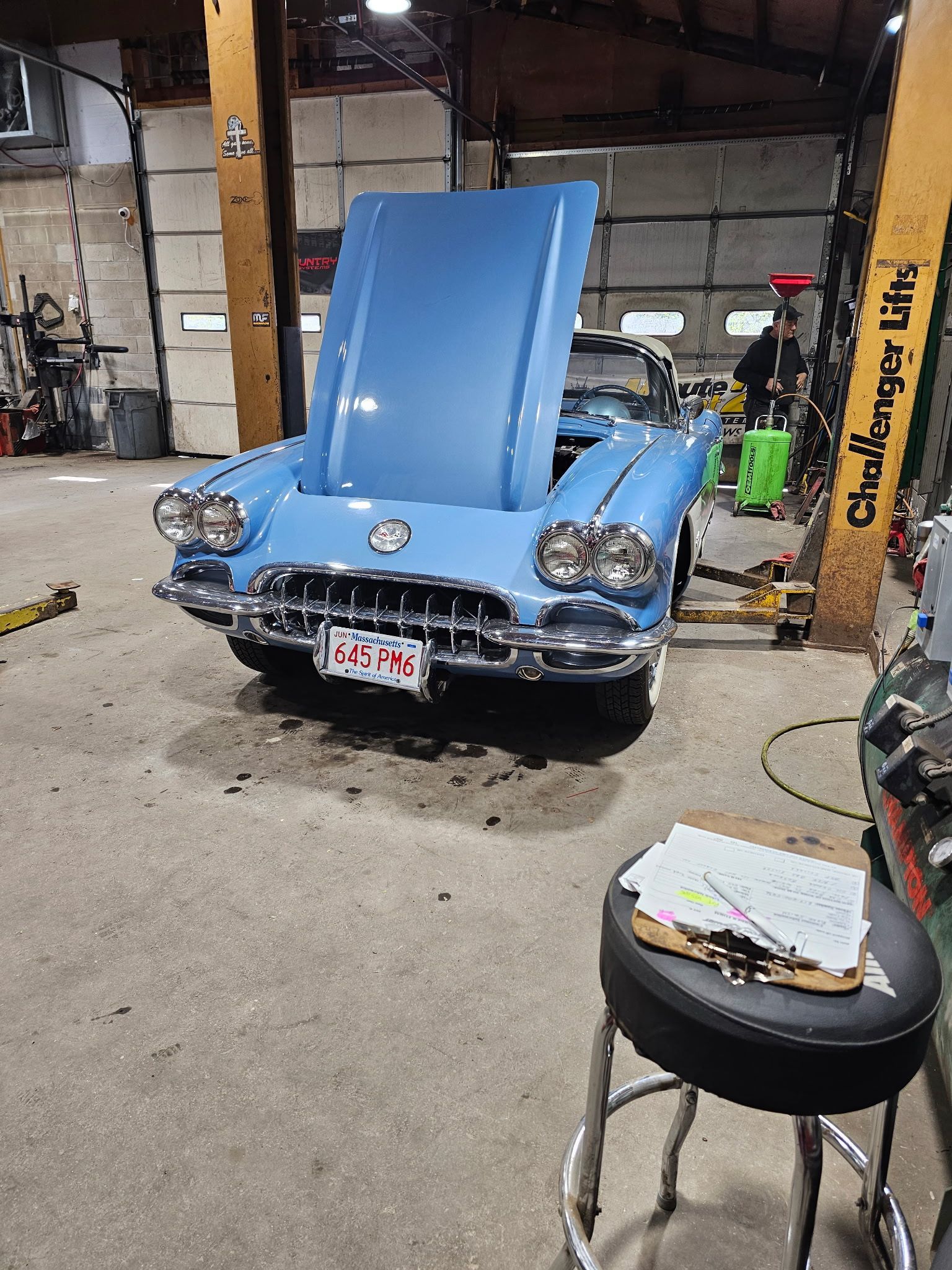 Blue classic car with hood open in a garage, seen from the front.