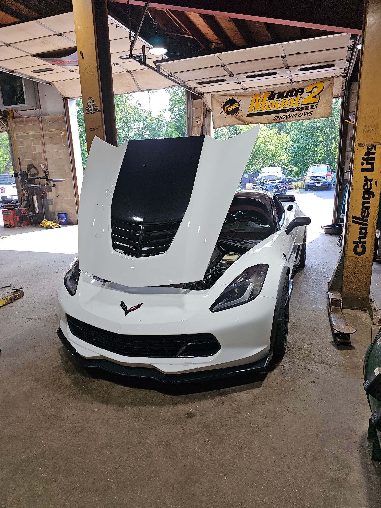 White sports car with raised hood in a garage, showing the engine bay.