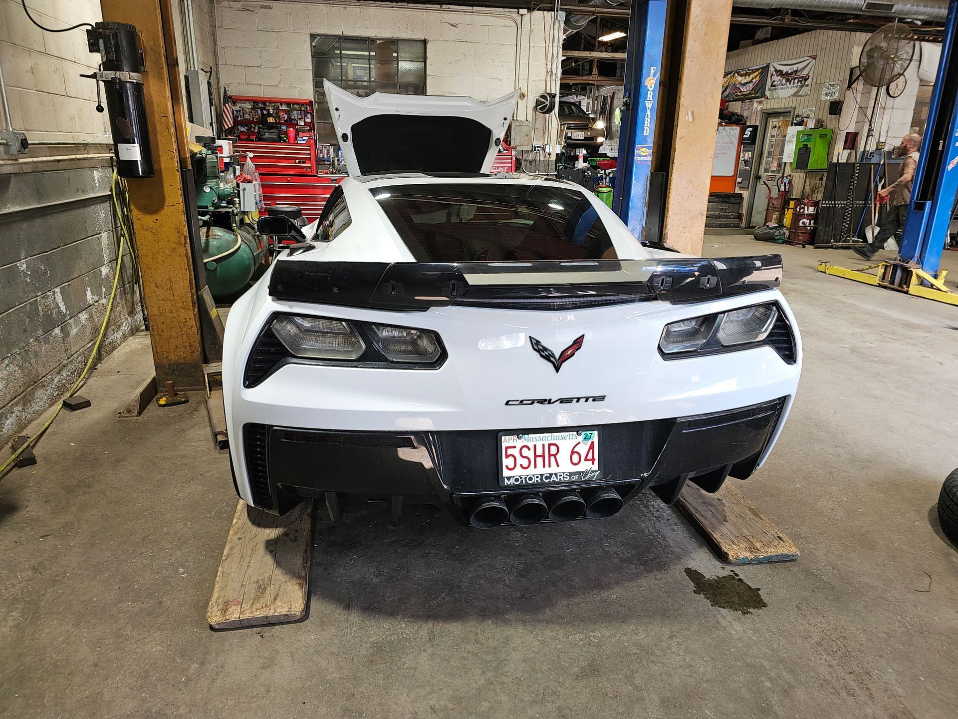 White Chevrolet Corvette on a lift in an auto shop, rear view with license plate visible