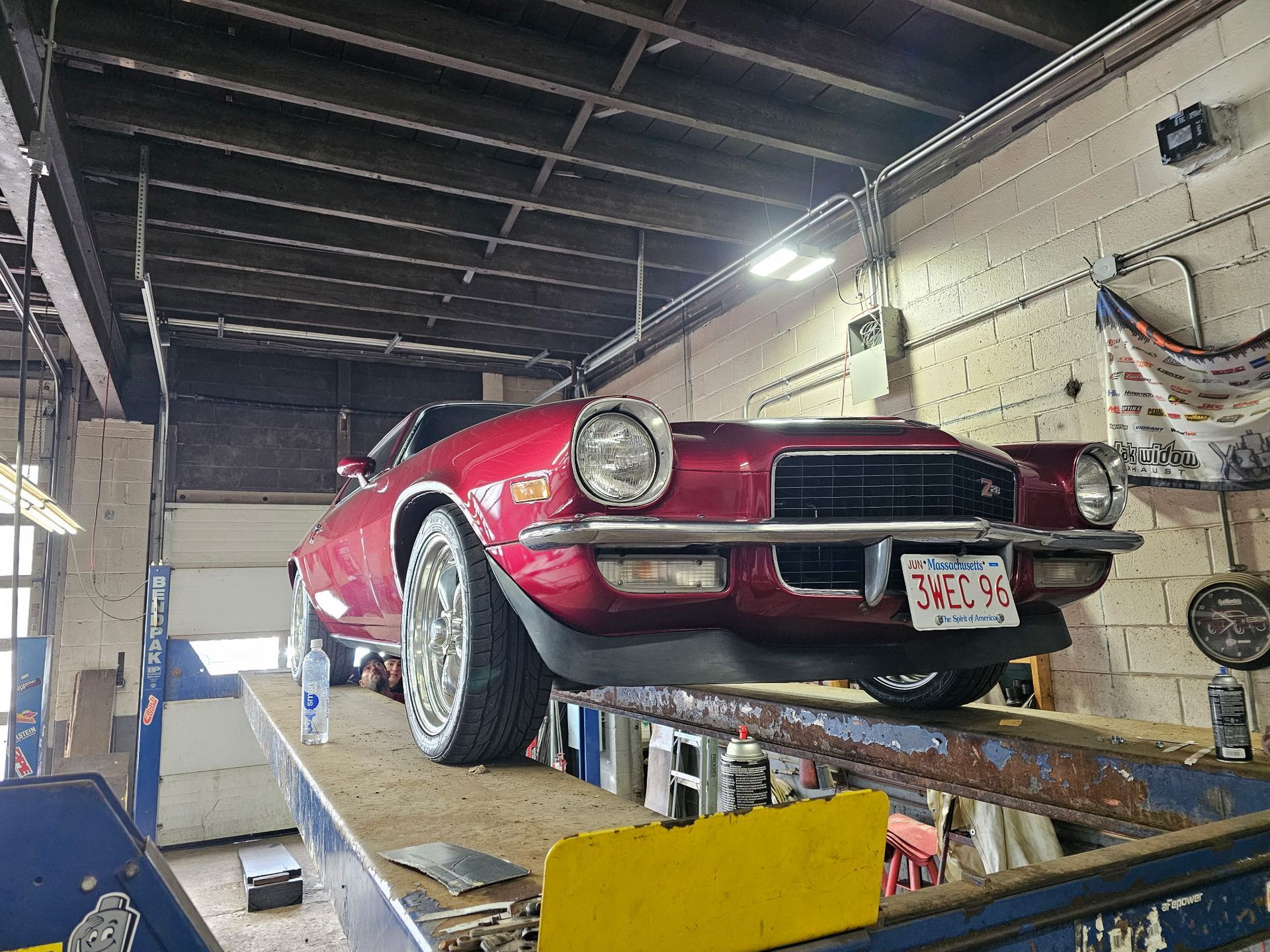 Red classic car on a lift in a garage, front view with white wheels and hood open